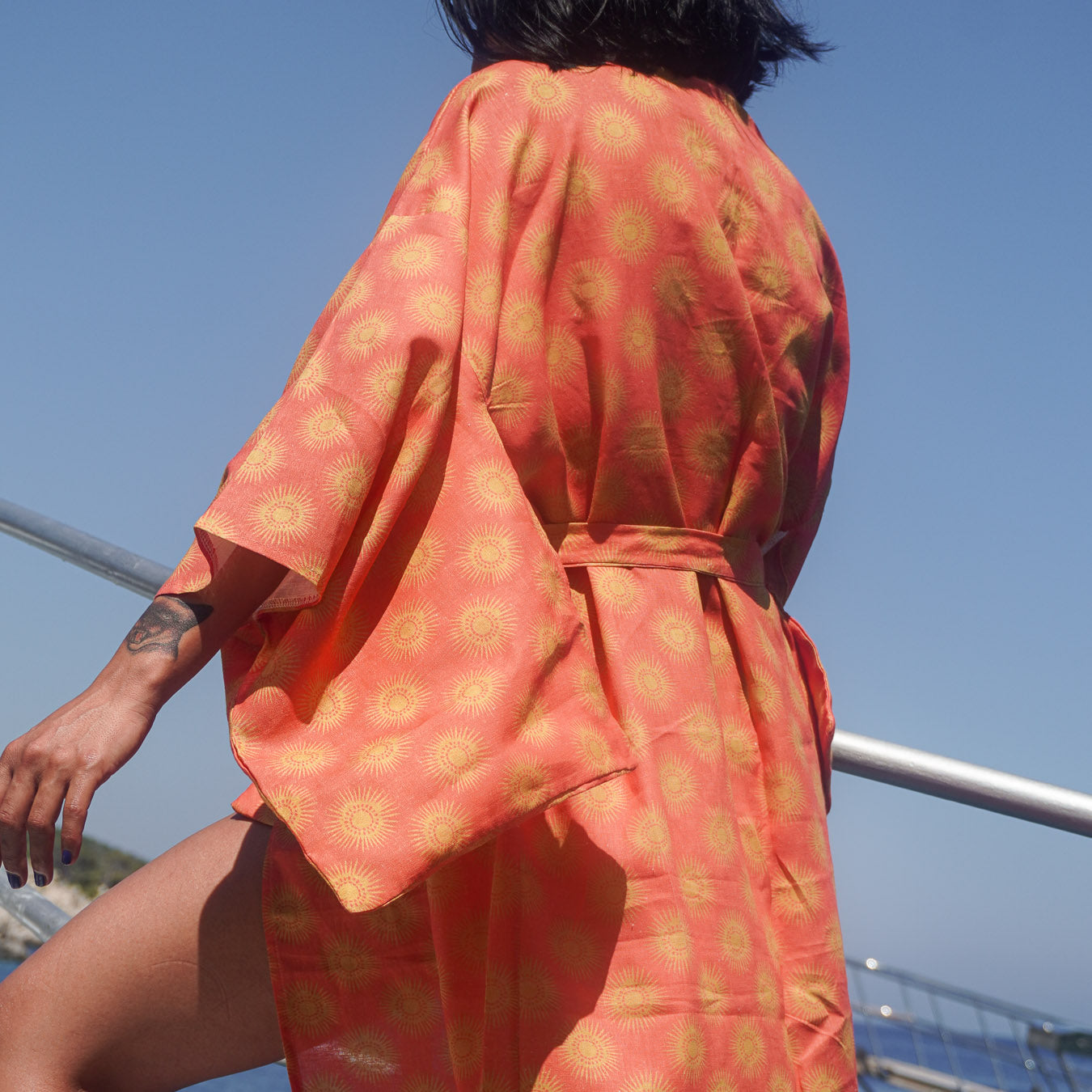 Person wearing a orange and gold sun patterned kimono against a blue sky.